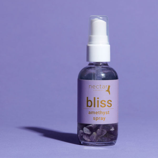 Vertical close-up of the small amber essential oil bottle against a vibrant purple background. The label is clearly visible, showing the white text 'bliss amethyst spray' oriented vertically.