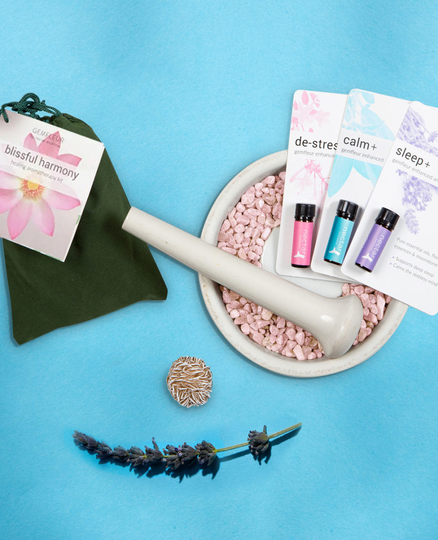 A product image featuring a selection of items including a green gemstone, a white mortar and pestle, pink crystals, a small round metal container, and three small bottles with colorful liquids, all arranged on a blue background.