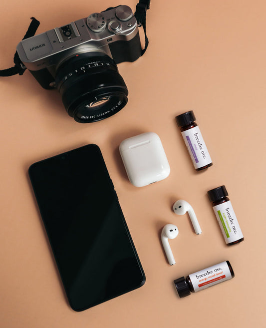 A flat lay of travel-related items including a camera, a smartphone, earbuds, essential oil bottles of breathe me jetsetter kit, and supplements.