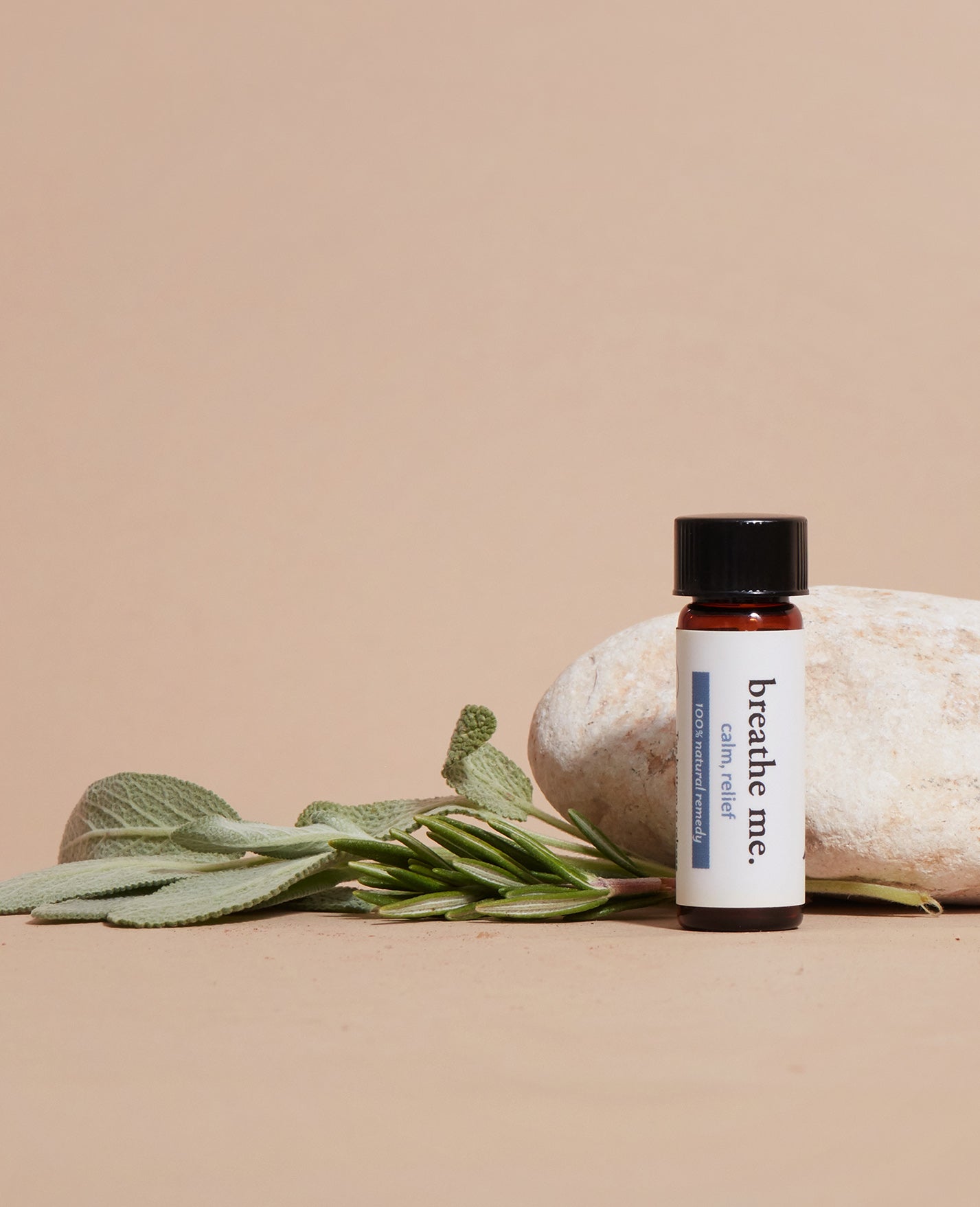 Bottle of 'breathe me' essential oil calm, relief with leaves and a rock on a beige background