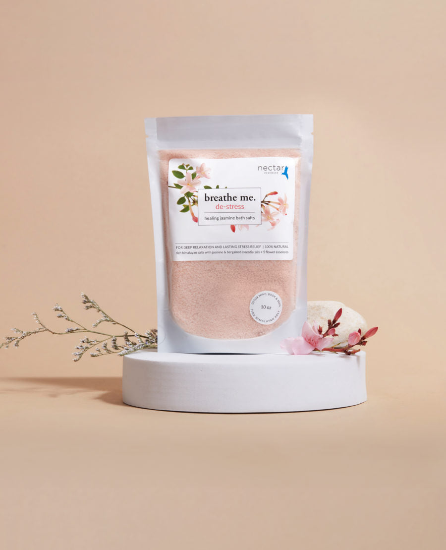 A package of 'de-stress healing bath salt' with a label showing jasmine flowers, placed on a white surface with a sprig of jasmine and a pink flower to the side.