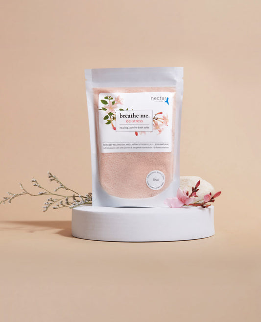 A package of 'de-stress healing bath salt' with a label showing jasmine flowers, placed on a white surface with a sprig of jasmine and a pink flower to the side.