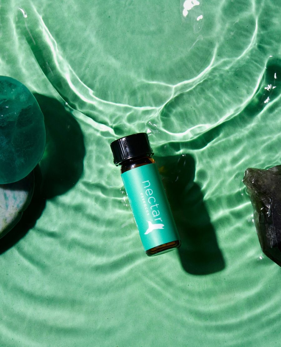A small bottle of essential oil labeled 'nectar' floating on green water, surrounded by a splash of water and a few leaves.