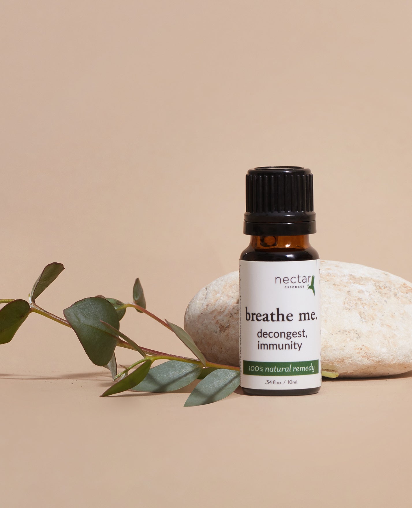 Nectar Remedies 'breathe me' essential oil bottle with eucalyptus leaves and a rock on a beige background