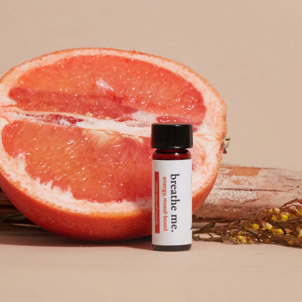 Breathe me essential oil energy mood boost bottel behind half cut orange, herb and wooden piece