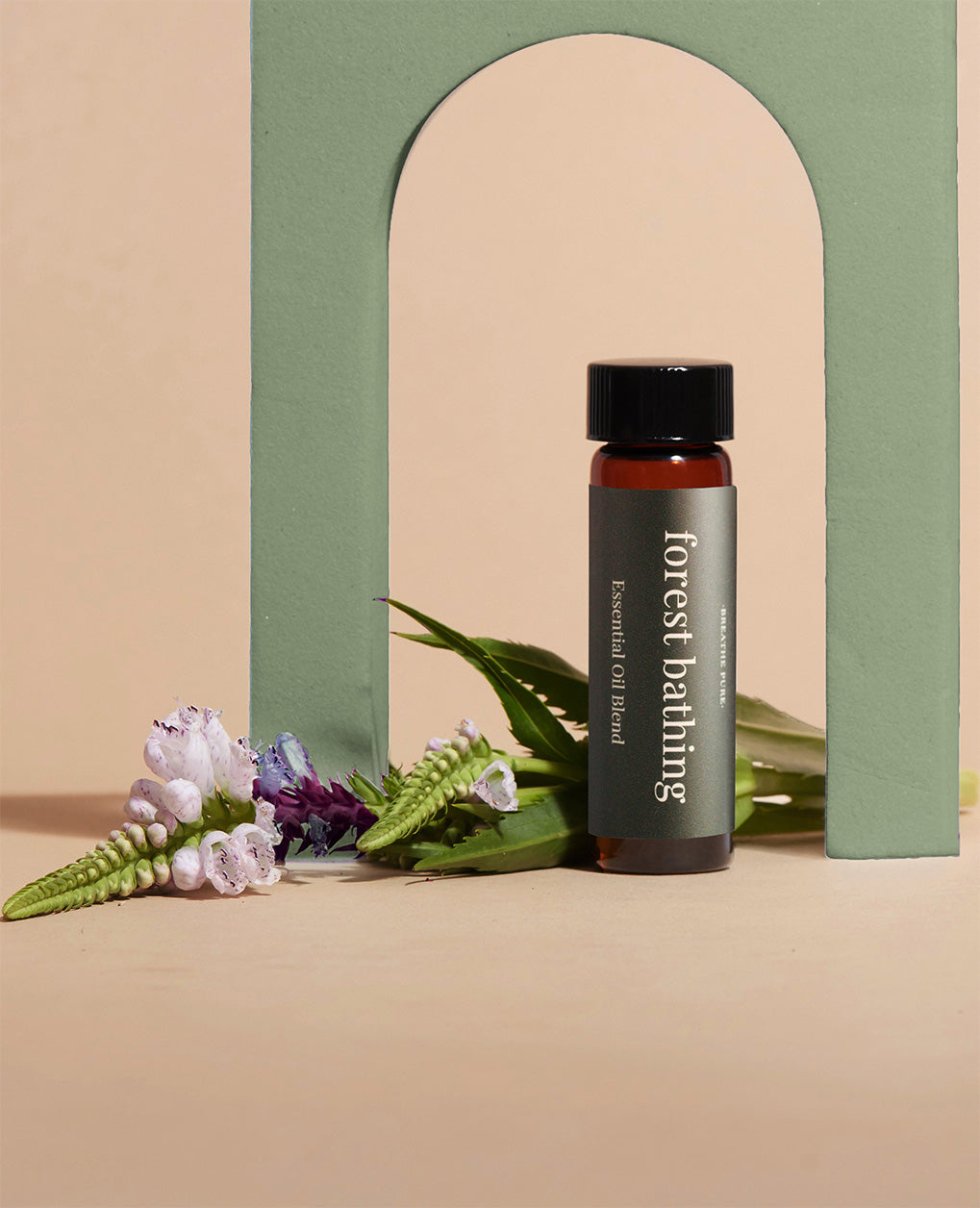 Stylized product shot of Forest Bathing essential oil bottle next to a sage green arch and forest-themed wildflowers.