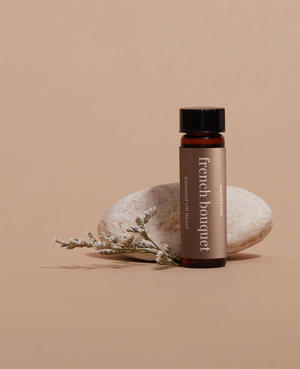 French Bouquet aromatherapy oil bottle displayed next to a smooth stone and delicate dried white floral sprig.