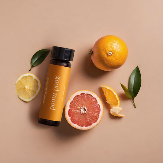 A bottle of 'good mood diffuser oil' with citrus fruits and leaves around it on a beige background.