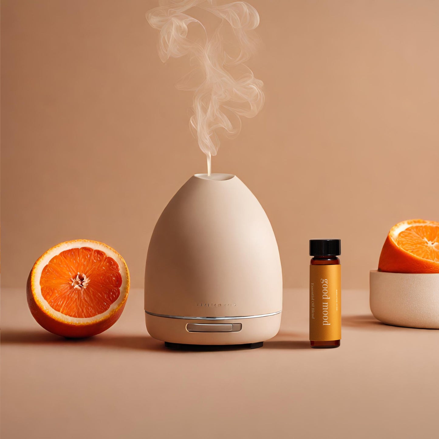Neutral-toned diffuser emitting steam, placed next to the 'good mood' essential oil bottle and two halves of a blood orange on a soft peach background.