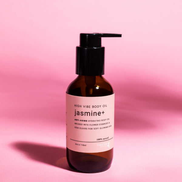 High Vibe Jasmine Plus Anti-Aging Hydrating Body Oil in an amber glass pump bottle on a solid pink background.