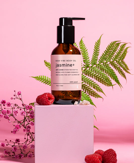 A bottle of body oil with a label that reads 'jasmine+', surrounded by flowers and berries on a pink background.