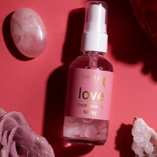 Nectar spray bottel laying on pink suface with white gem and rose and pink rose and also diomond rock.