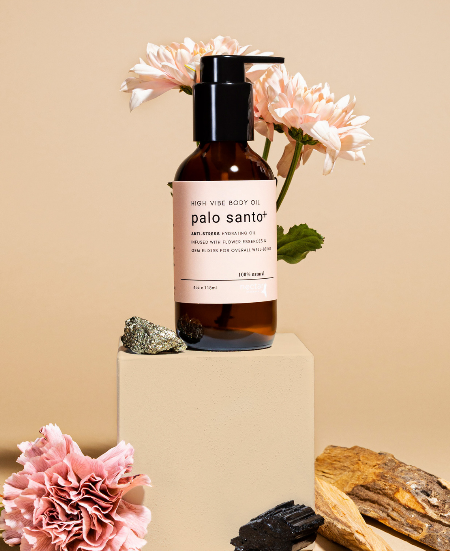 A clear bottle of Palo Santo body oil with a pump dispenser, placed on a beige pedestal. The label has 'palo santo' written on it.