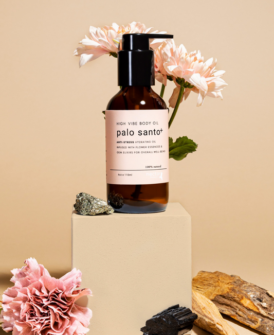 A clear bottle of Palo Santo body oil with a pump dispenser, placed on a beige pedestal. The label has 'palo santo' written on it.