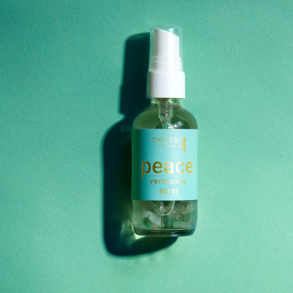 Vertical close-up of the small amber essential oil bottle against a vibrant blue background. The label is clearly visible, showing the white text 'peace vermarine spray' oriented vertically.