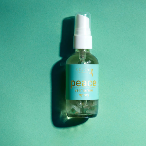 Laying Vertical close-up of the small amber essential oil bottle against a vibrant blue background. The label is clearly visible, showing the white text 'peace vermarine spray' oriented vertically.