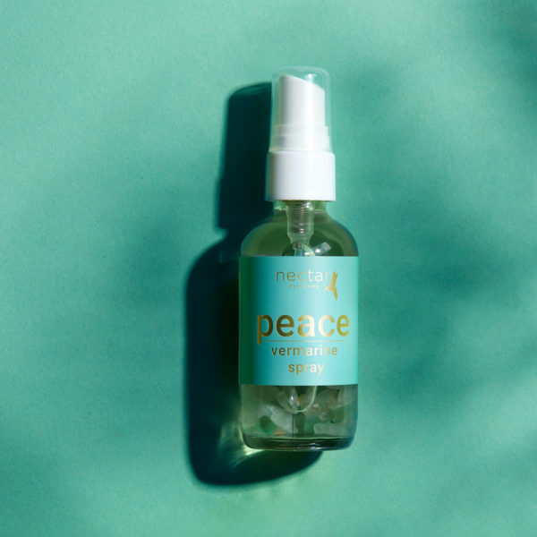 Vertical centered close-up of the small amber essential oil bottle against a vibrant laying background. The label is clearly visible, showing the white text 'pece vermanrine spray' oriented vertically.