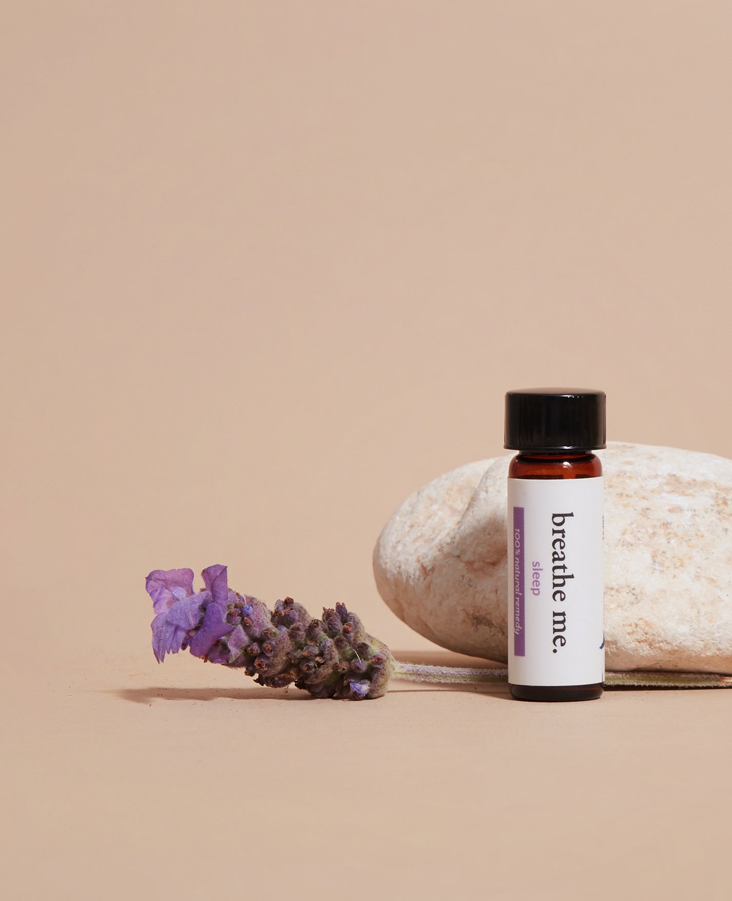 Essential oil sleep bottle labeled 'breathe me' with lavender and a rock on a beige background