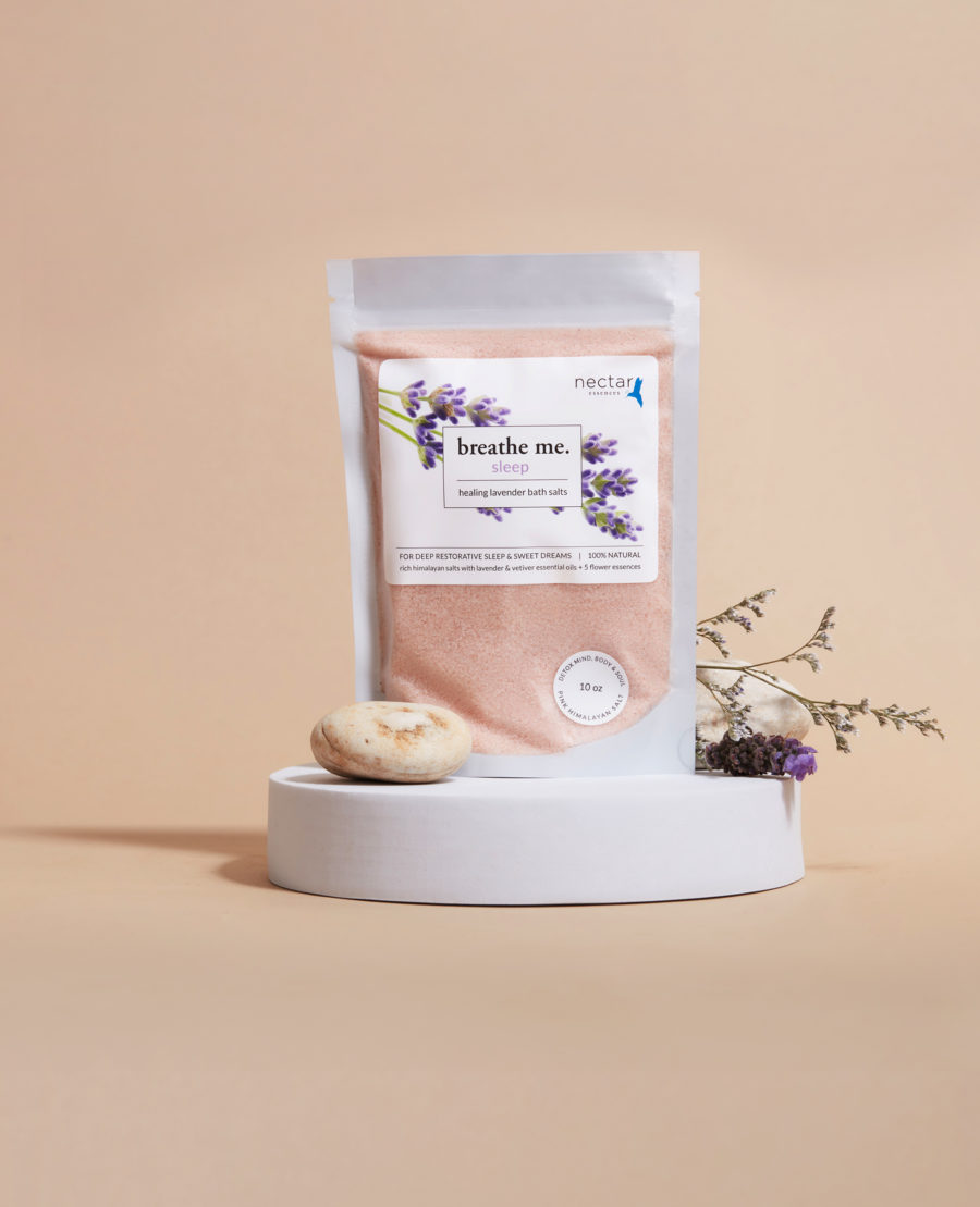A pouch of sleep healing bath salt with lavender oil and pink himalayan salt, presented on a white platform with decorative dry flowers beside it.