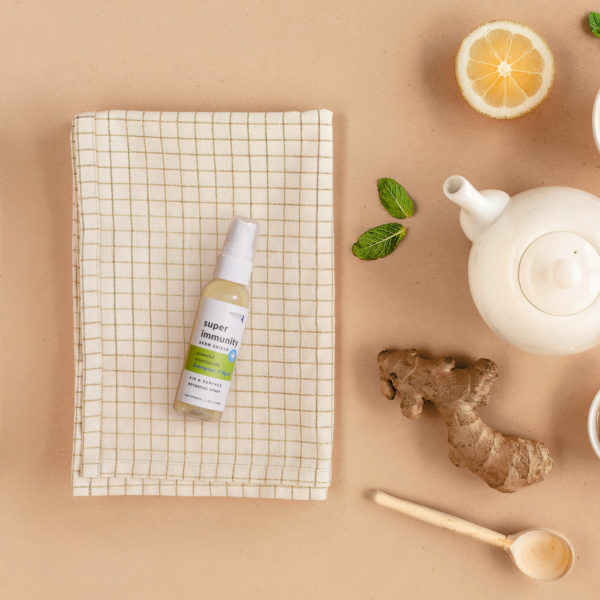A spray bottles arranged on a surface with  lifted on checkered piece of cloth lemon slices, mint leaves, and a teapot, suggesting a theme of natural wellness and immunity boosting.