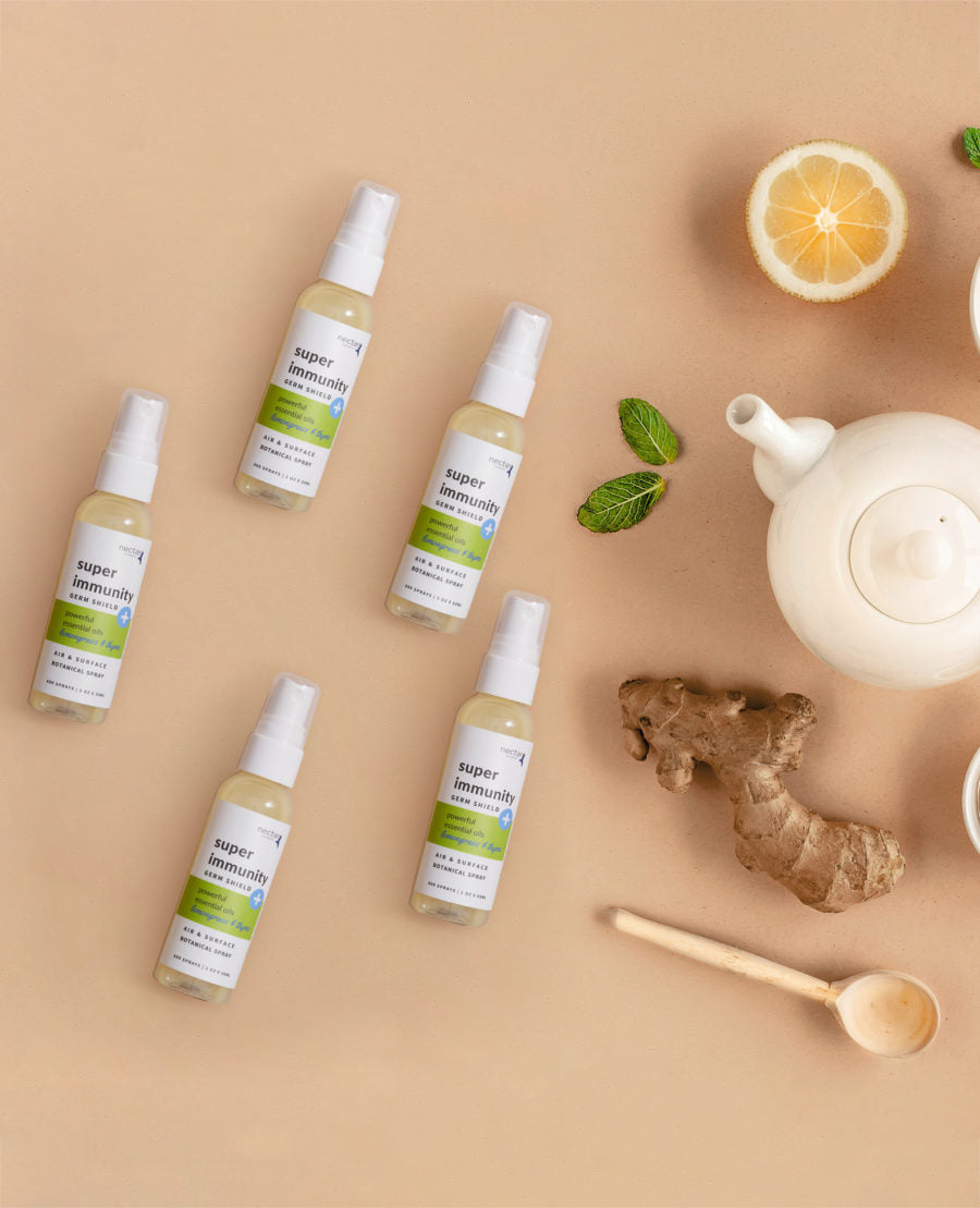 Five small spray bottles arranged on a surface with lemon slices, mint leaves, and a teapot, suggesting a theme of natural wellness and immunity boosting.