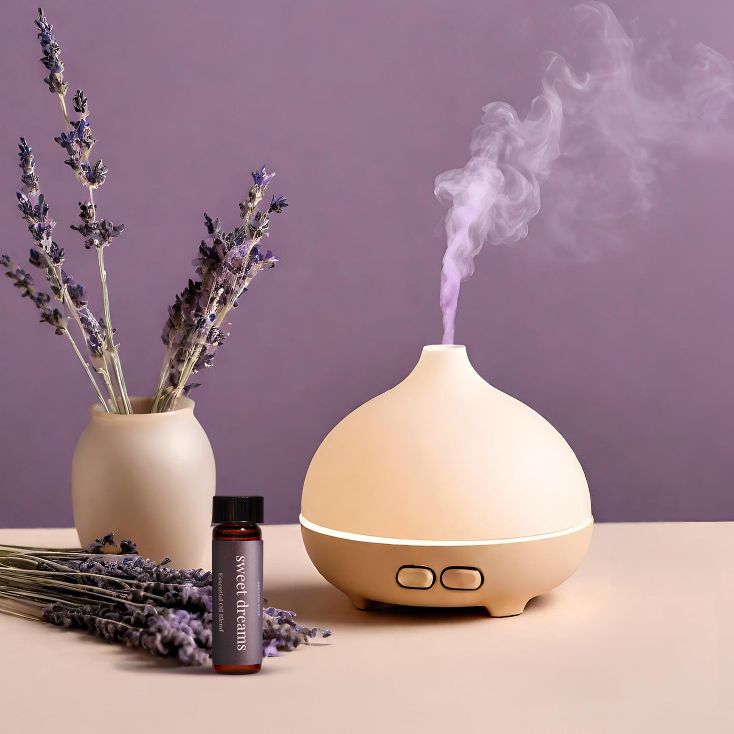 Sweet Dreams essential oil bottle next to a beige aromatherapy diffuser emitting purple steam, styled with a vase of dried lavender flowers.