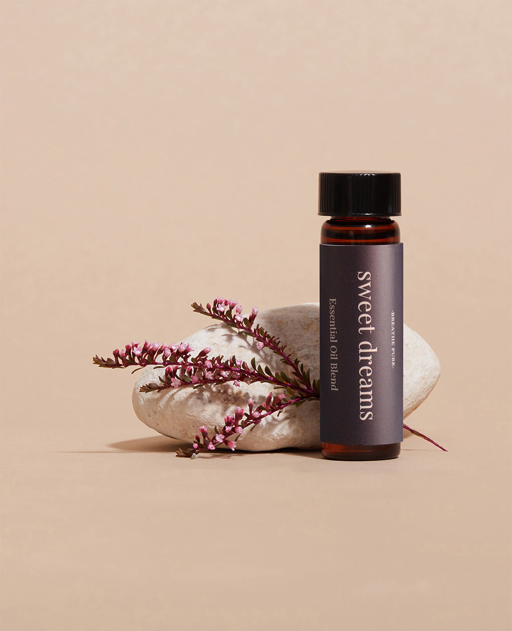Sweet Dreams essential oil bottle displayed next to a smooth white stone and delicate purple heather flowers