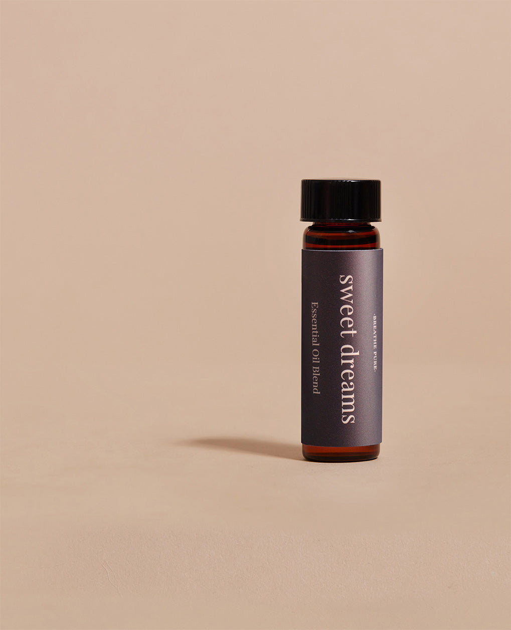 Close-up of Sweet Dreams essential oil blend glass bottle with a dark purple label on a simple beige background.