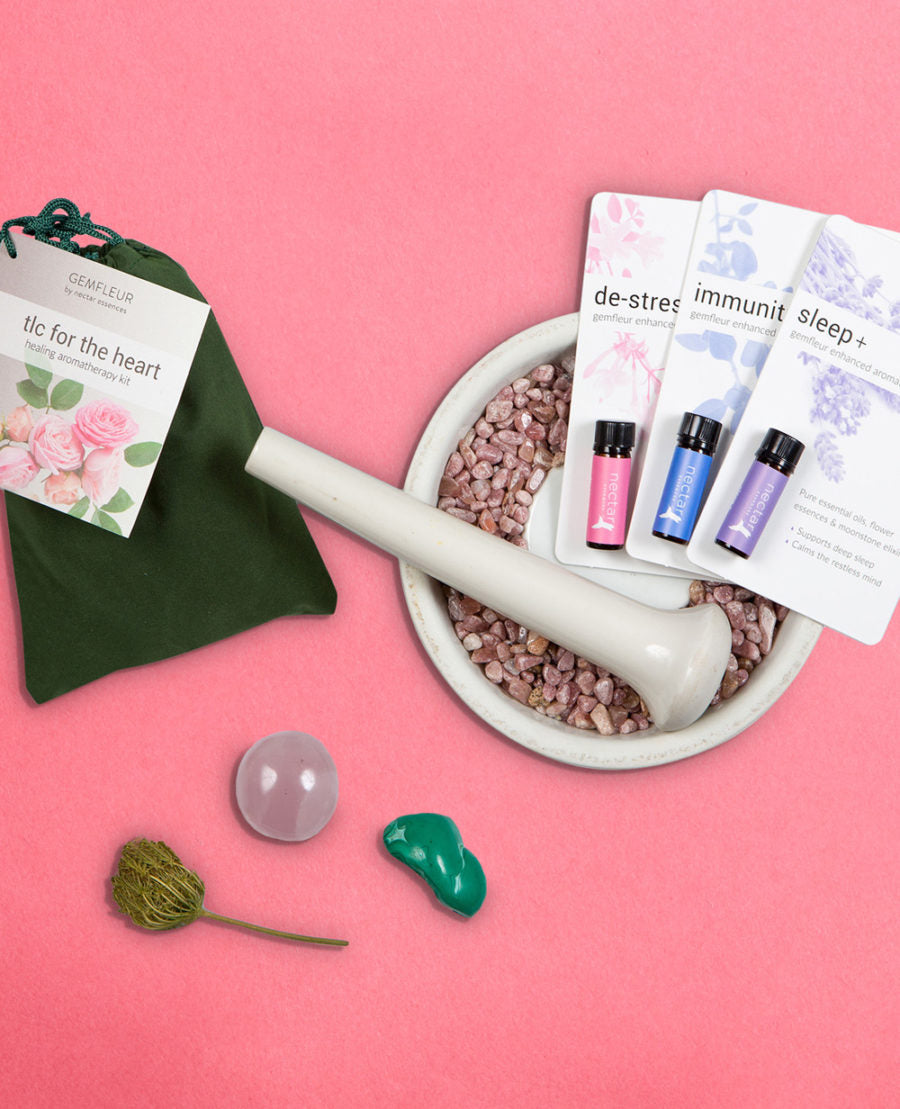 A collection of items including a green pouch, a white mortar and pestle, purple and pink essence bottles, a clear round item, and a green heart-shaped object, all arranged on a pink background.