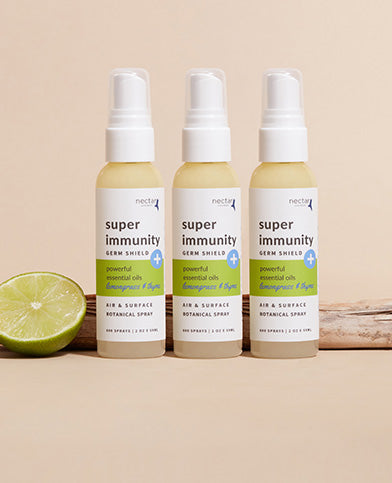 Three spray bottles labeled 'super immunity germ shield spray', accompanied by a slice of lemon and placed on a wooden surface.