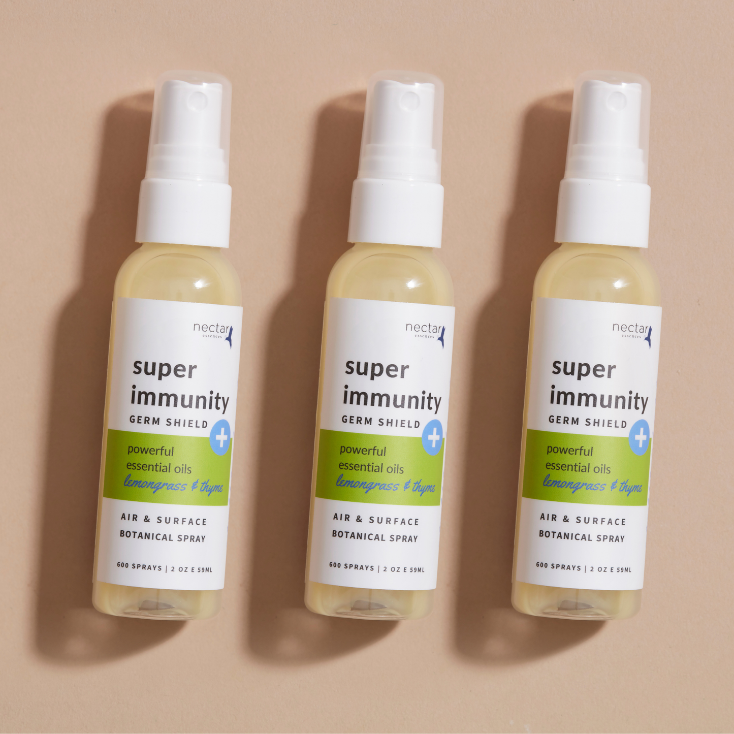Three spray bottles labeled 'super immunity germ shield spray' laying on beige background