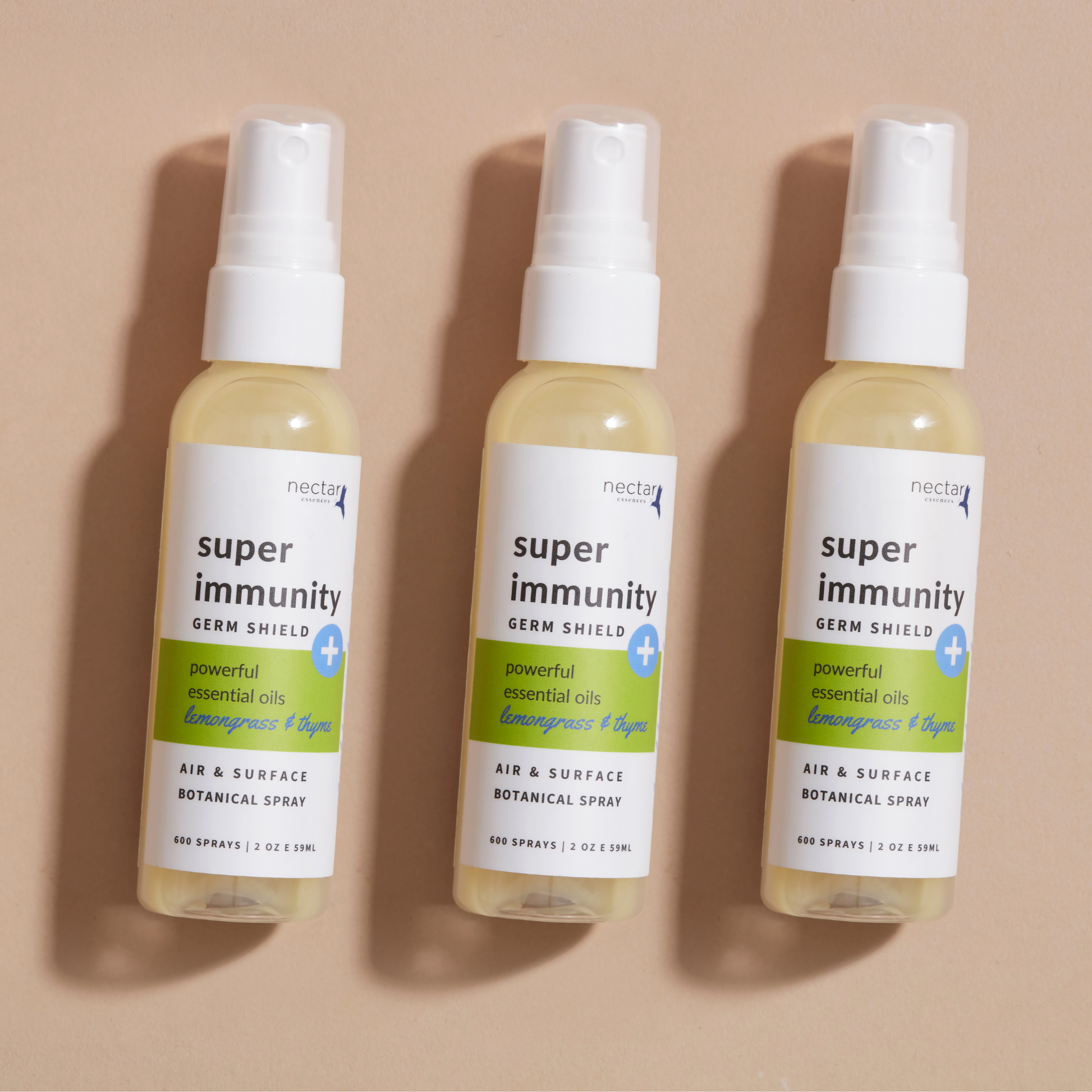 Three spray bottles labeled 'super immunity germ shield spray' laying on beige background