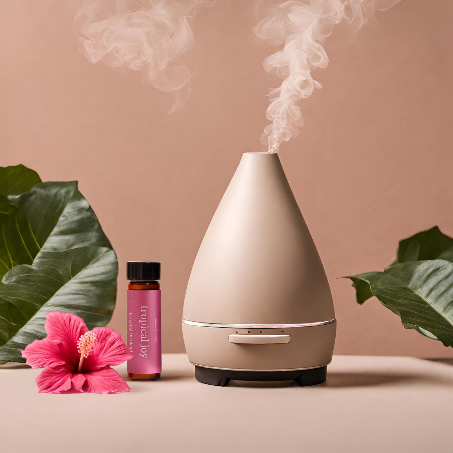Neutral-toned essential oil diffuser emitting steam, placed next to the 'tropical joy' oil bottle and a bright pink hibiscus flower, with large tropical leaves in the background.