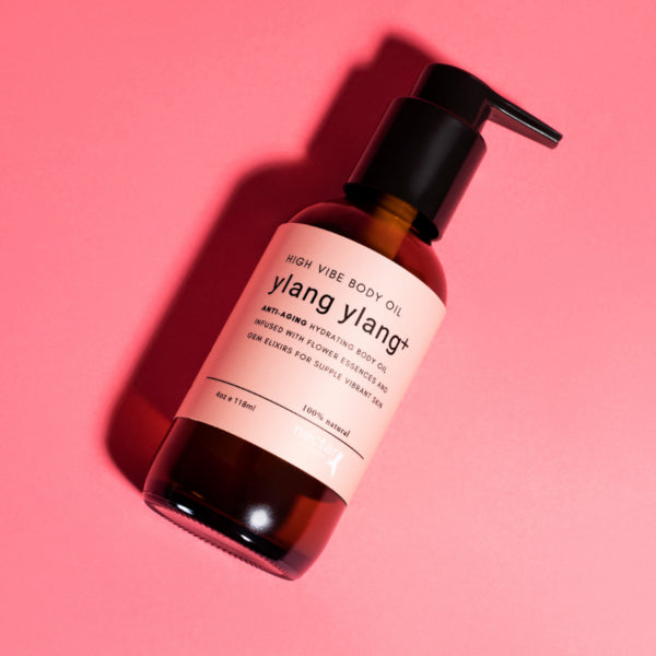 Angled shot of High Vibe Ylang Ylang+ Body Oil bottle on a pink surface highlighting the anti-aging formula for supple, vibrant skin.