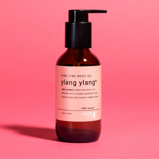 High Vibe Ylang Ylang Plus Anti-Aging Hydrating Body Oil in an amber glass pump bottle on a vibrant pink background