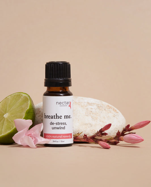 A bottle labeled 'Nectar Essences Breathe Me Stress Unwind' with a few drops of liquid, a lime, a pink flower, and a piece of cheese to the side, on a beige background.