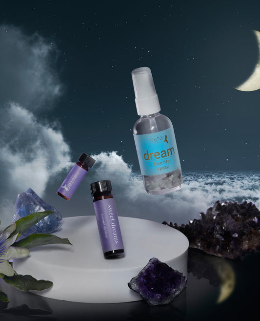 A aromatherapy kit including a spray bottle labeled 'dream', two small bottles of essential oils, and surrounding by what appears to be lavender plants and crystals, presented against a night sky backdrop.